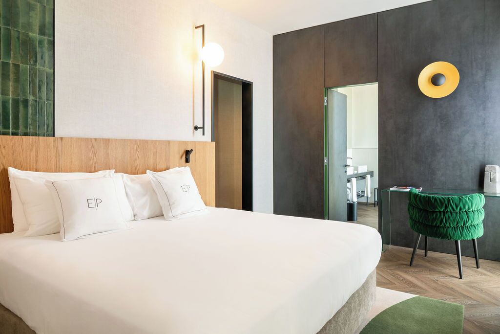 Ein modernes Hotelzimmer mit einem großen Bett, einem grünen Polsterstuhl und einem Spiegel an der Wand.