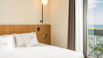 A hotel room with a bed, pillows with 'EIP' text, a nightstand, a wall-mounted light, and a view of the outdoors.