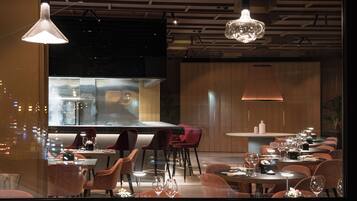 A modern restaurant with a long dining table, multiple chairs, and pendant lighting.