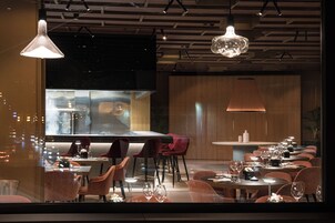 A modern restaurant with a long dining table, multiple chairs, and pendant lighting.