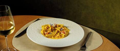 A plate of pasta with a glass of white wine on a wooden table.