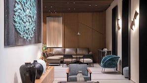 Un salon moderne avec un canapé, des fauteuils et une table basse. Un grand tableau abstrait orne le mur, et un vase est posé sur la table d’appoint.