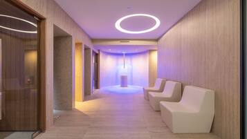 A modern hallway with a reception desk, a massage chair, and a wall-mounted massage pod.