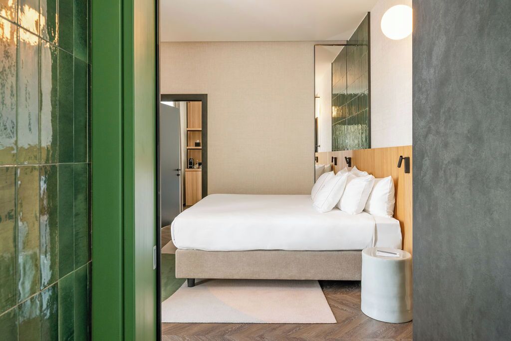 A modern bedroom with a large bed, a bedside table, a mirror, and a green-framed door.
