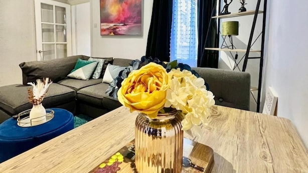 Una sala de estar con una mesa de centro de madera, un jarrón con flores y una mesita auxiliar azul.