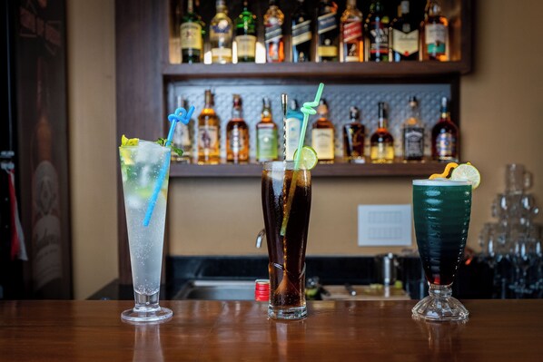 Three cocktails on a bar counter with a shelf of liquor bottles in the background. - Triple Crown Resort (Baireni)