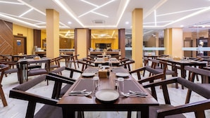 Un comedor espacioso con varias mesas y sillas, iluminación moderna y una cocina visible al fondo.