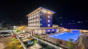 Un hotel de varios pisos con piscina, mobiliario exterior y zona de estacionamiento.