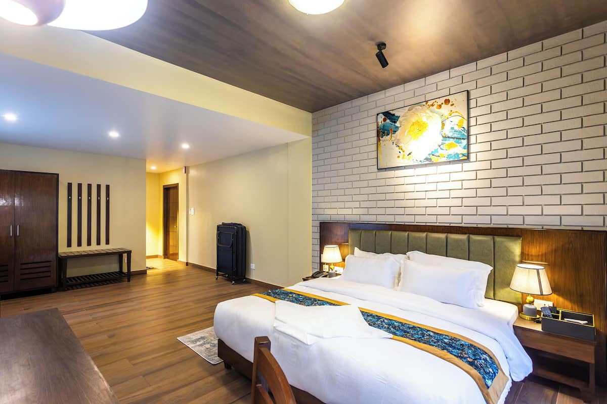 Habitación de hotel con una cama grande, piso de madera, un banco, un escritorio y una obra de arte colgada en la pared.