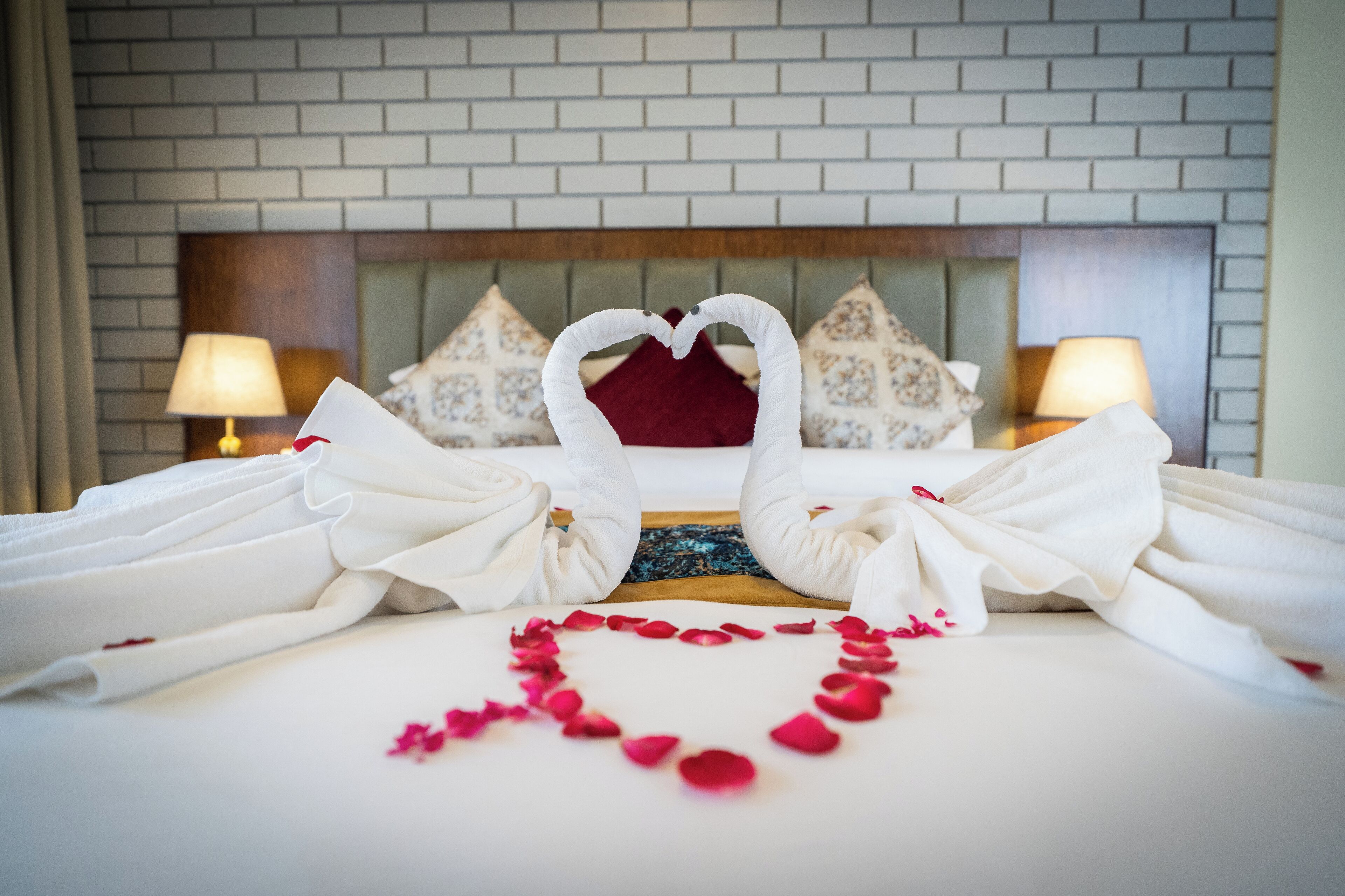 A hotel room with a neatly made bed, a heart-shaped arrangement of rose petals, and towels folded into a heart shape.