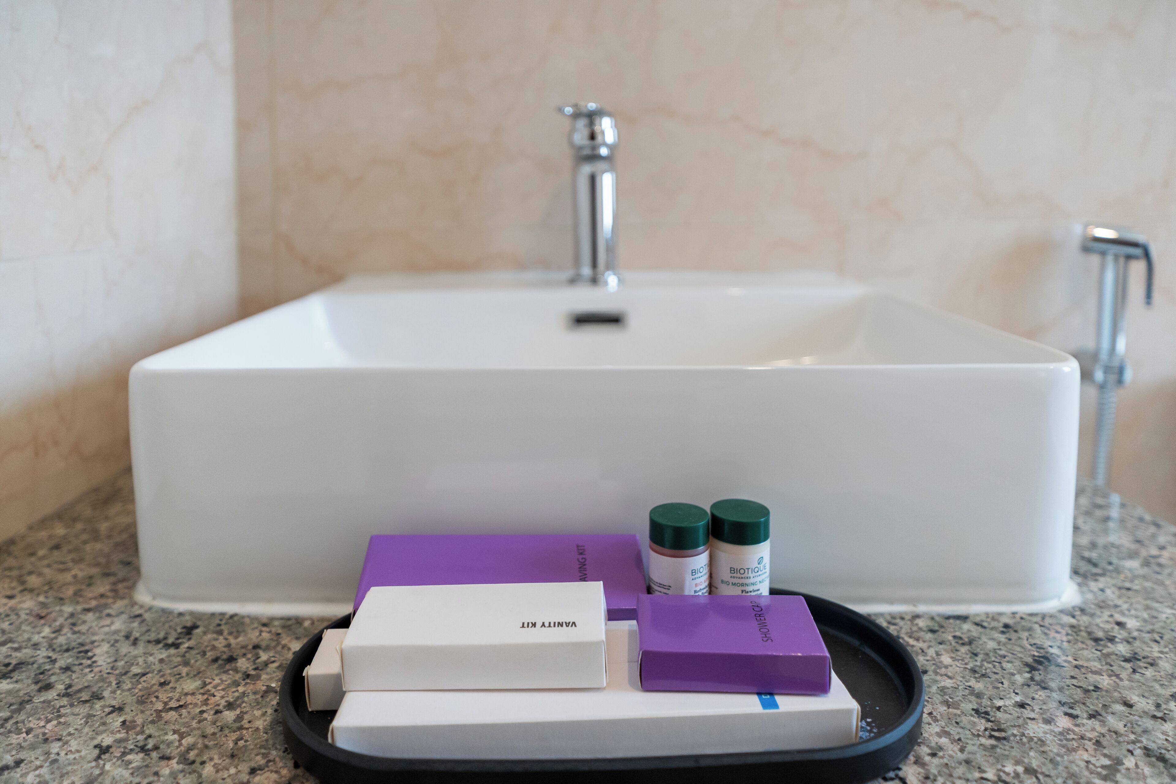 A bathroom sink with a marble wall, a tray with a white box labeled "VANTLY KIT," and two green-capped bottles.
