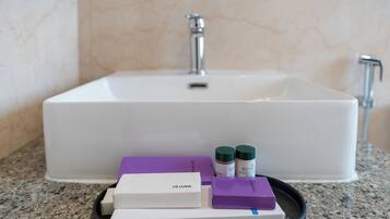 A bathroom sink with a marble wall, a tray with a white box labeled "VANTLY KIT," and two green-capped bottles.