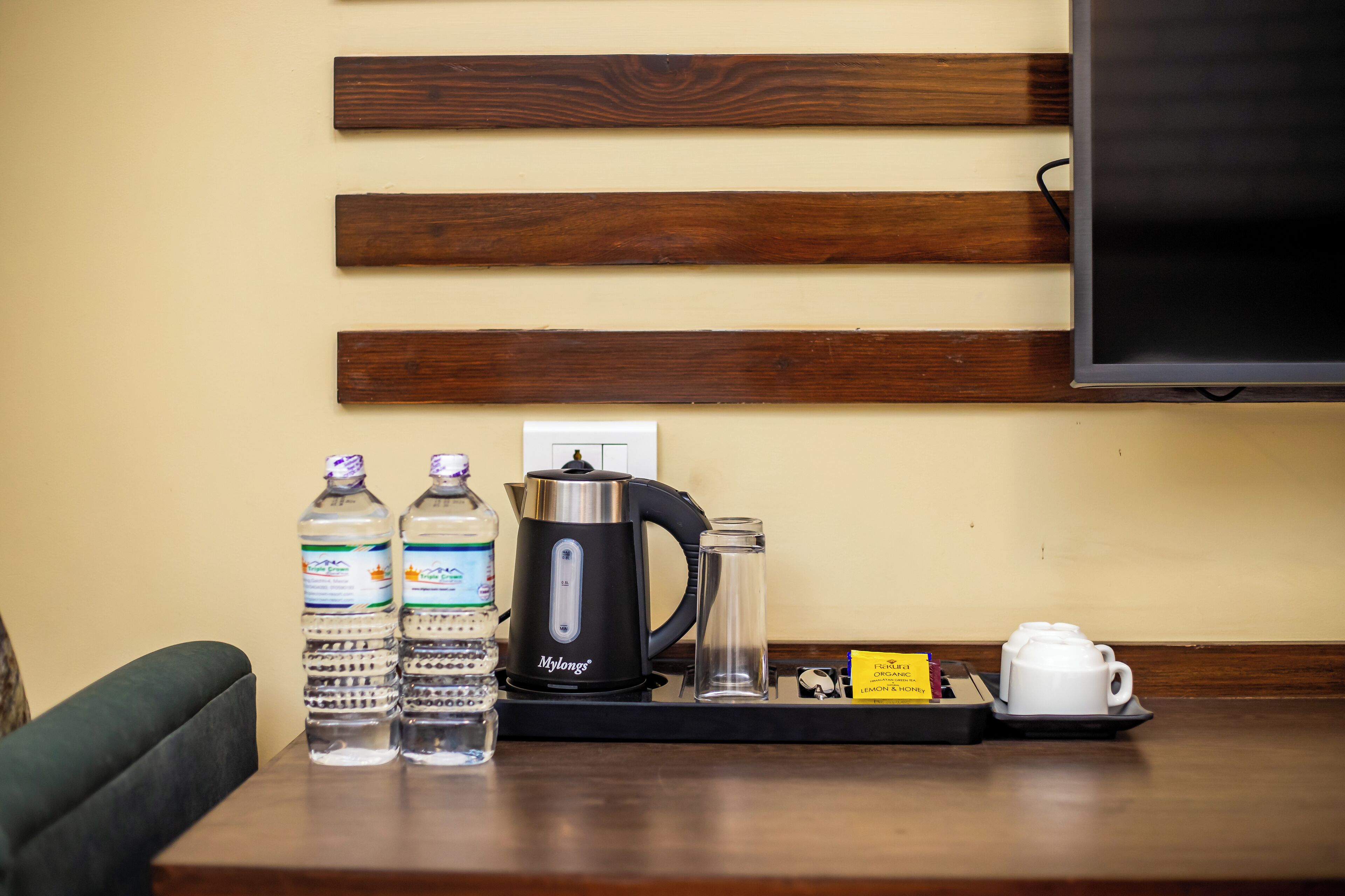 A coffee station with water bottles, a coffee maker, a glass, and a teapot on a wooden table.