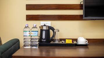 A coffee station with water bottles, a coffee maker, a glass, and a teapot on a wooden table.