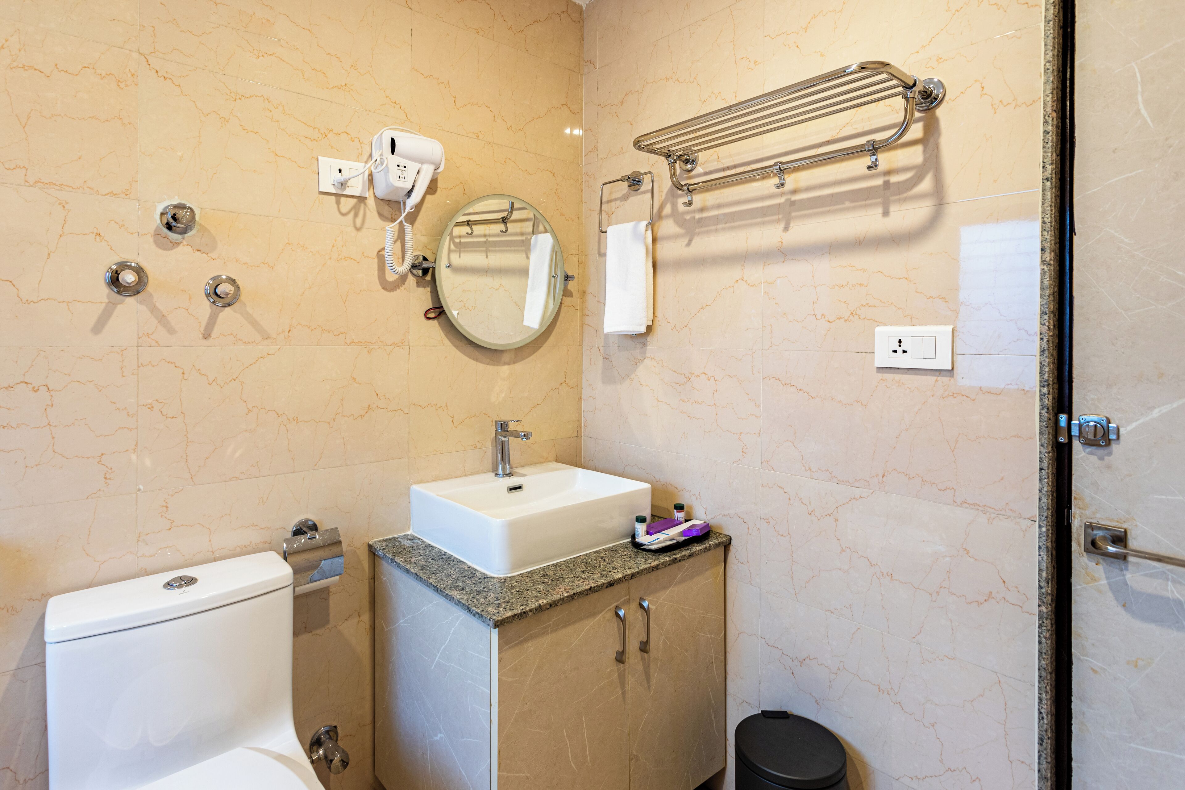A bathroom with a sink, mirror, towel rack, and a hairdryer on the wall.