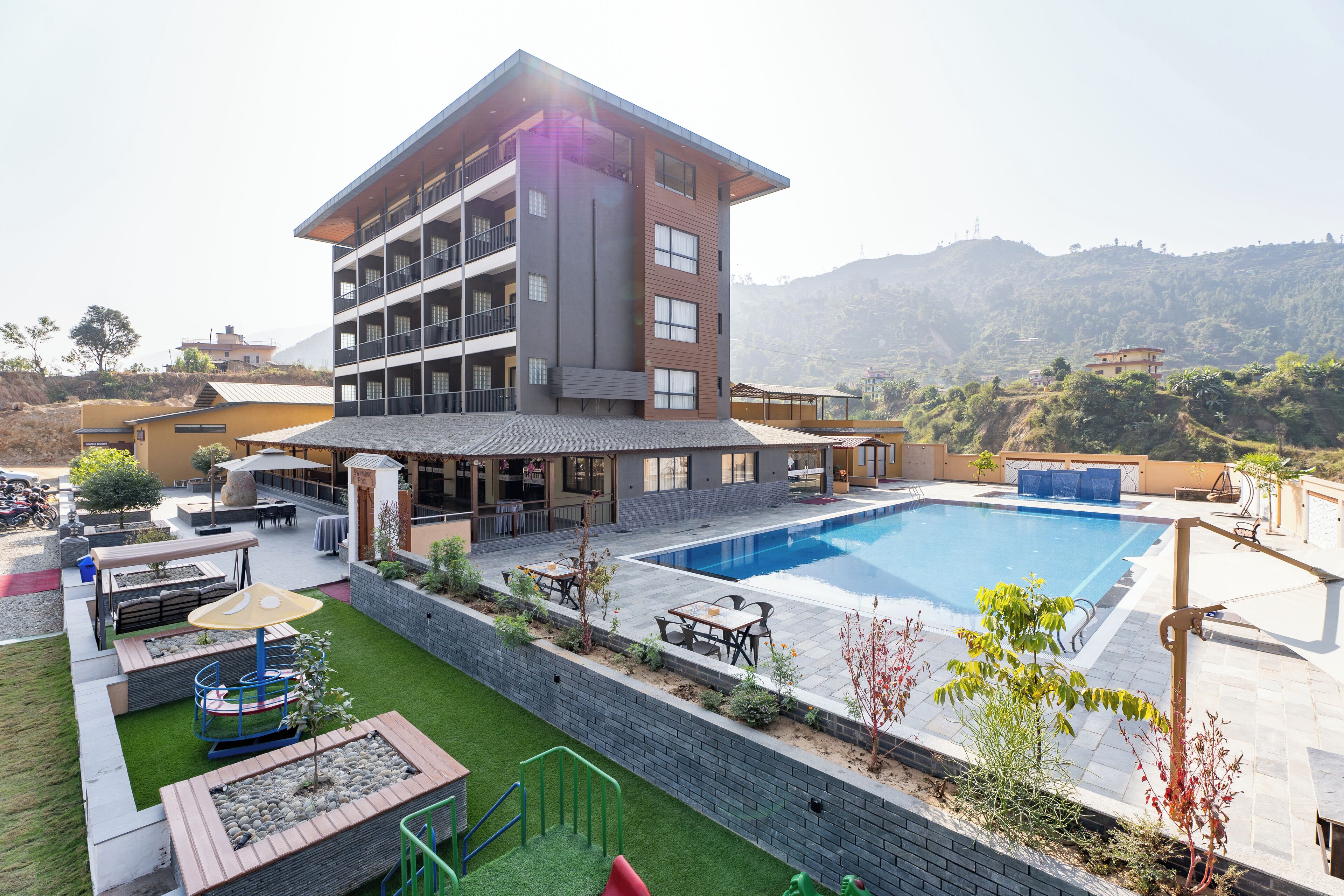 A modern hotel with a rooftop pool, outdoor seating, and a view of the surrounding hills.