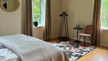 A bedroom with a bed, a chair, a small table, a mirror, and a window with curtains.