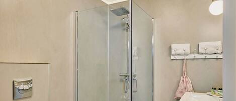 A bathroom with a toilet, a glass shower enclosure, patterned floor tiles, and a sink with a towel rack.