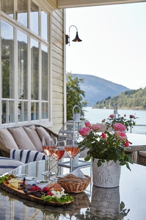 A table set with a cheese board, fruits, and glasses of rosé wine, overlooking a lake with mountains in the background. - Visnes hotel Stryn AS (Stryn)