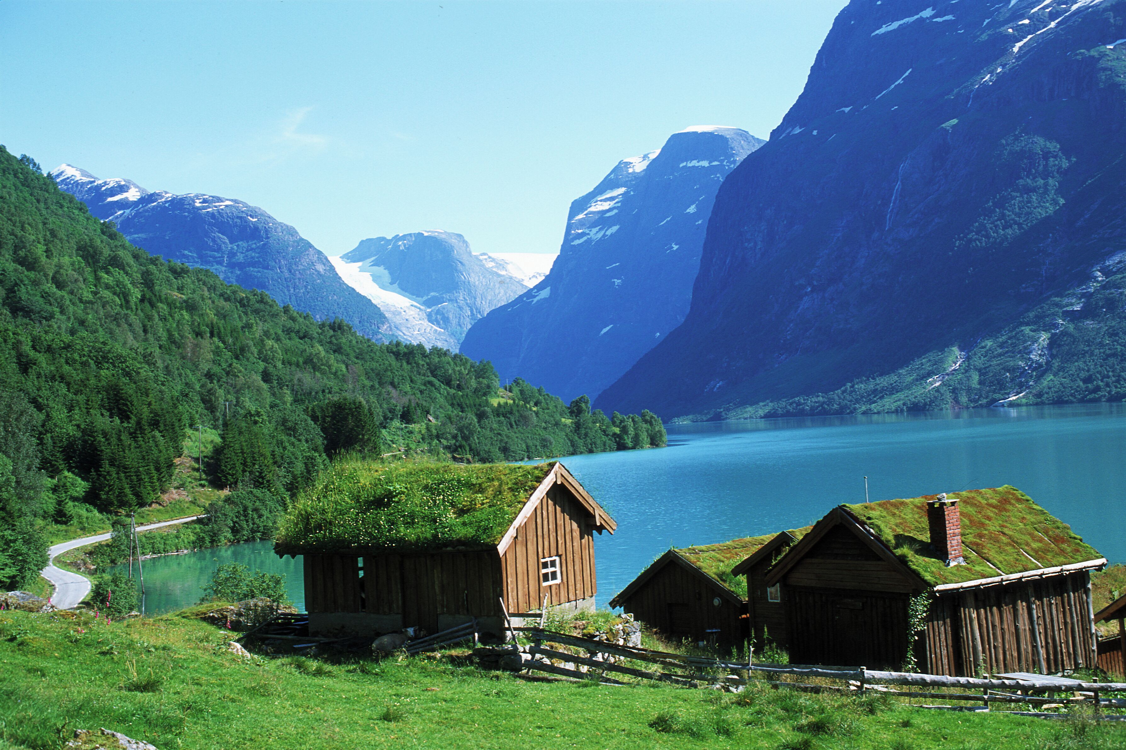 A mountain landscape with a lake, wooden cabins, and a winding road.
