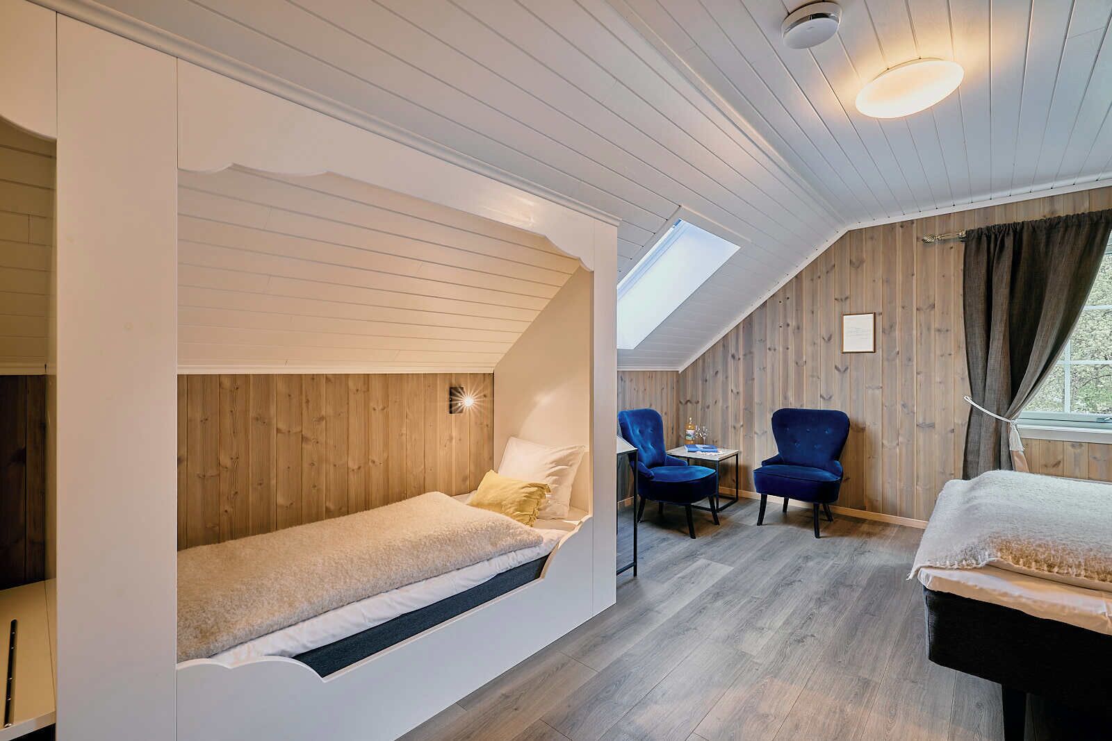 A cozy room with a loft bed, a small desk, two chairs, and a window with curtains.