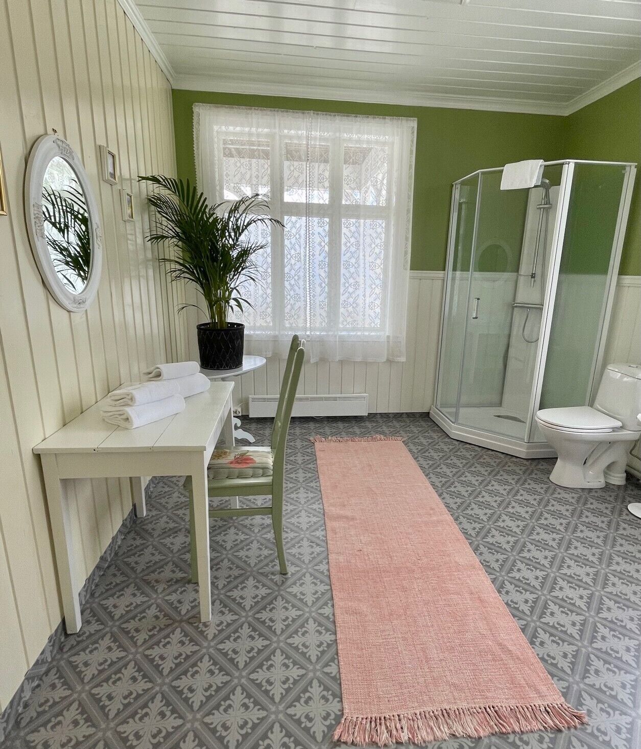 Un baño con ducha, inodoro, una mesa, una silla y una planta.