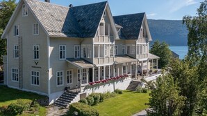 Een groot hotel met twee verdiepingen, een opvallend 'V' logo, een overdekte veranda en uitzicht op een meer.