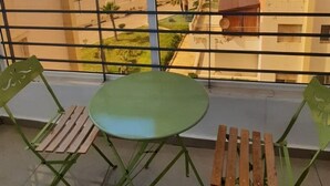 A balcony with a round table and two chairs, a metal railing, and a view of buildings and greenery. - 2-bedroom apartment for 6 people (Tanger)