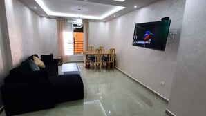 A modern living room with a sectional sofa, a dining table with chairs, and a flat-screen TV mounted on the wall. - 2-bedroom apartment for 6 people (Tanger)