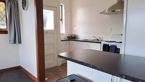 A modern kitchen with white cabinets, a black countertop, and a stainless steel range hood. There is a window with a curtain, a clock on the wall, and a small stool. - Spacious, Affordable, Peaceful Family Home (Dunedin)