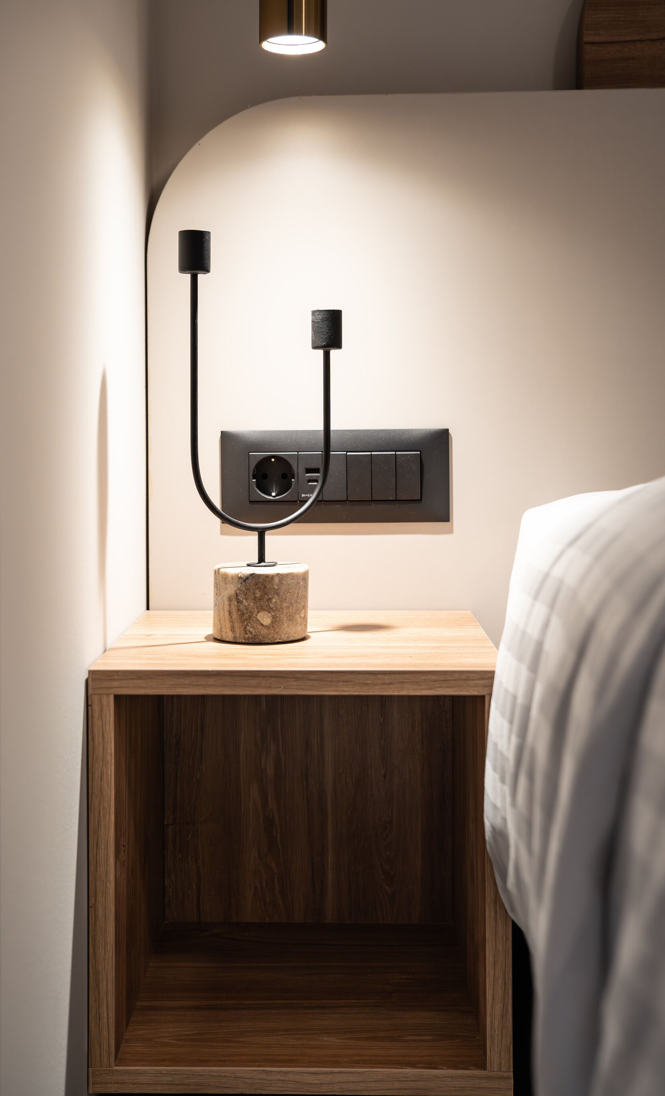 A wooden bedside table with a modern lamp and a power outlet.