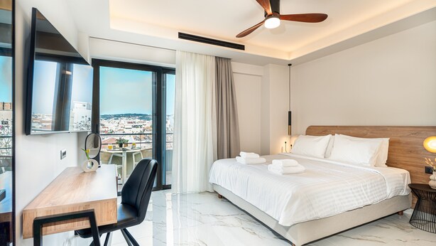 Une chambre d’hôtel moderne équipée d’un lit, d’un bureau, d’une chaise, d’un ventilateur de plafond et d’une grande fenêtre donnant sur la ville.