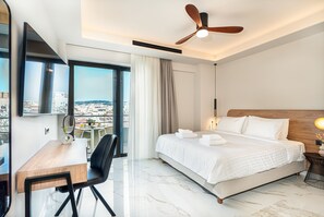 Una habitación de hotel moderna con cama, escritorio, silla, ventilador de techo y un amplio ventanal con vista a la ciudad.