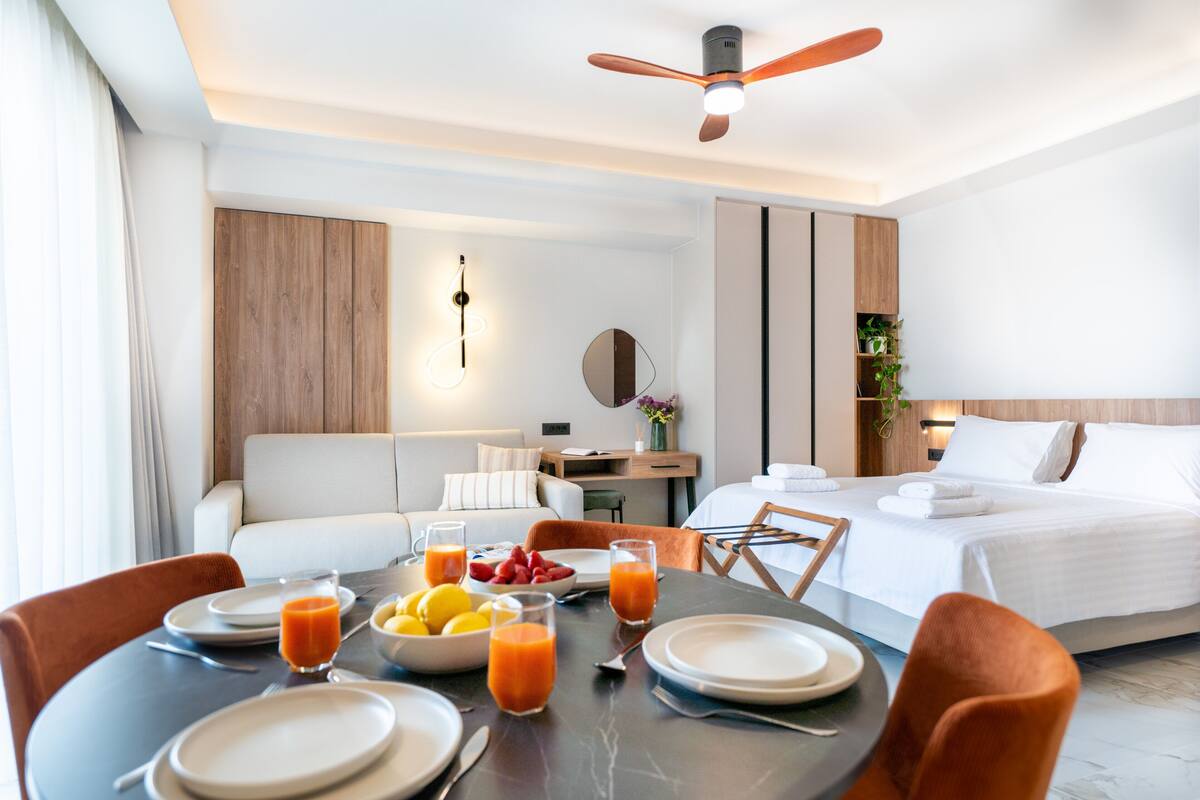A hotel room with a dining area, a bed, a ceiling fan, and a bedside table with a lamp.