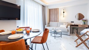 Une chambre d’hôtel moderne dotée d’un coin repas, d’un canapé, d’une télévision et d’un espace de travail.