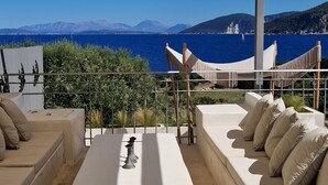 Una terrazza con un divano bianco, un tavolino e un'amaca sospesa. La terrazza si affaccia su un corpo d'acqua e montagne.