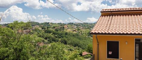A yellow building with a tiled roof, a fenced playground, and a view of a green hillside.
