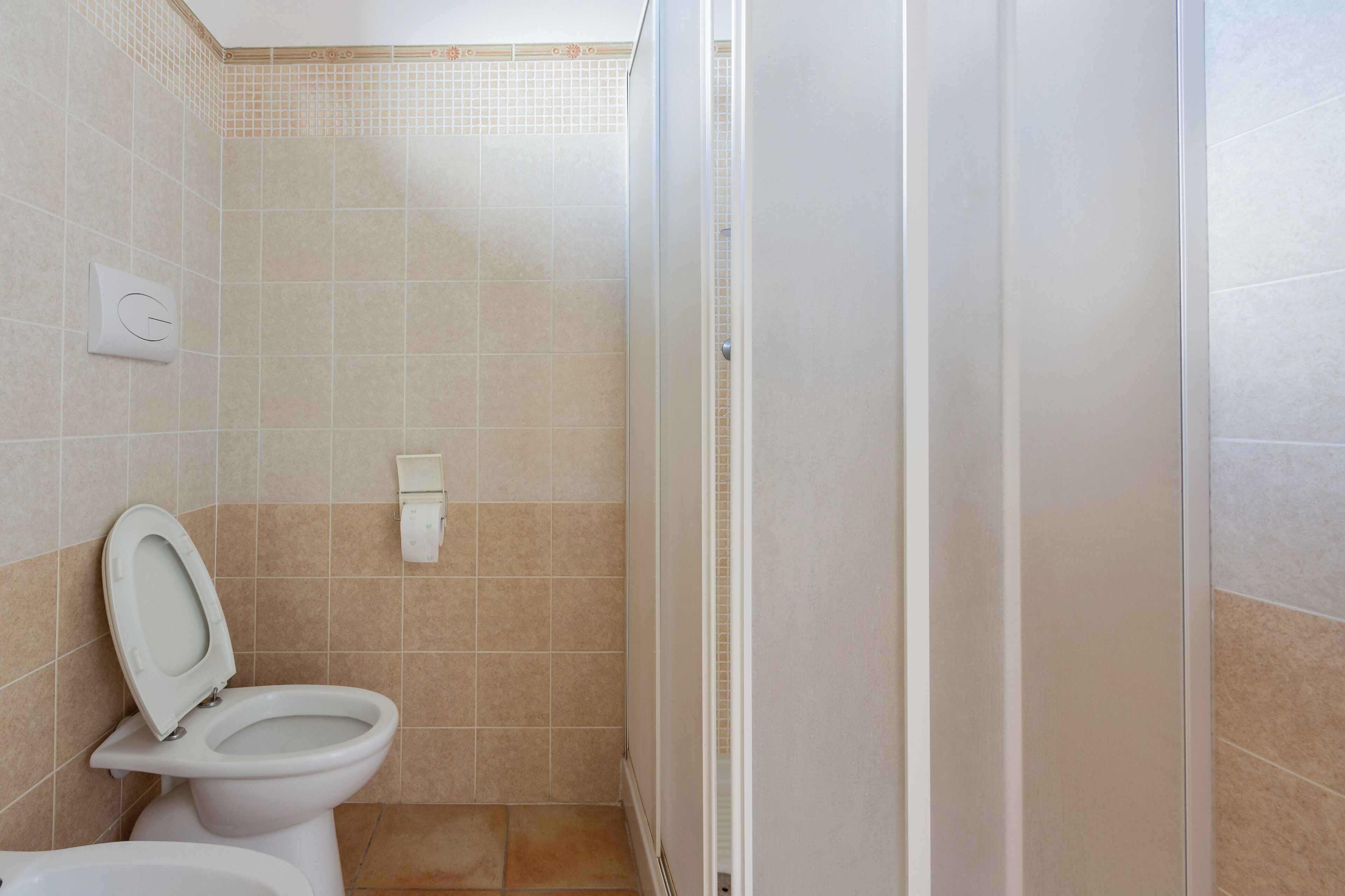 A bathroom with a toilet, a shower, and a wall-mounted hand dryer.