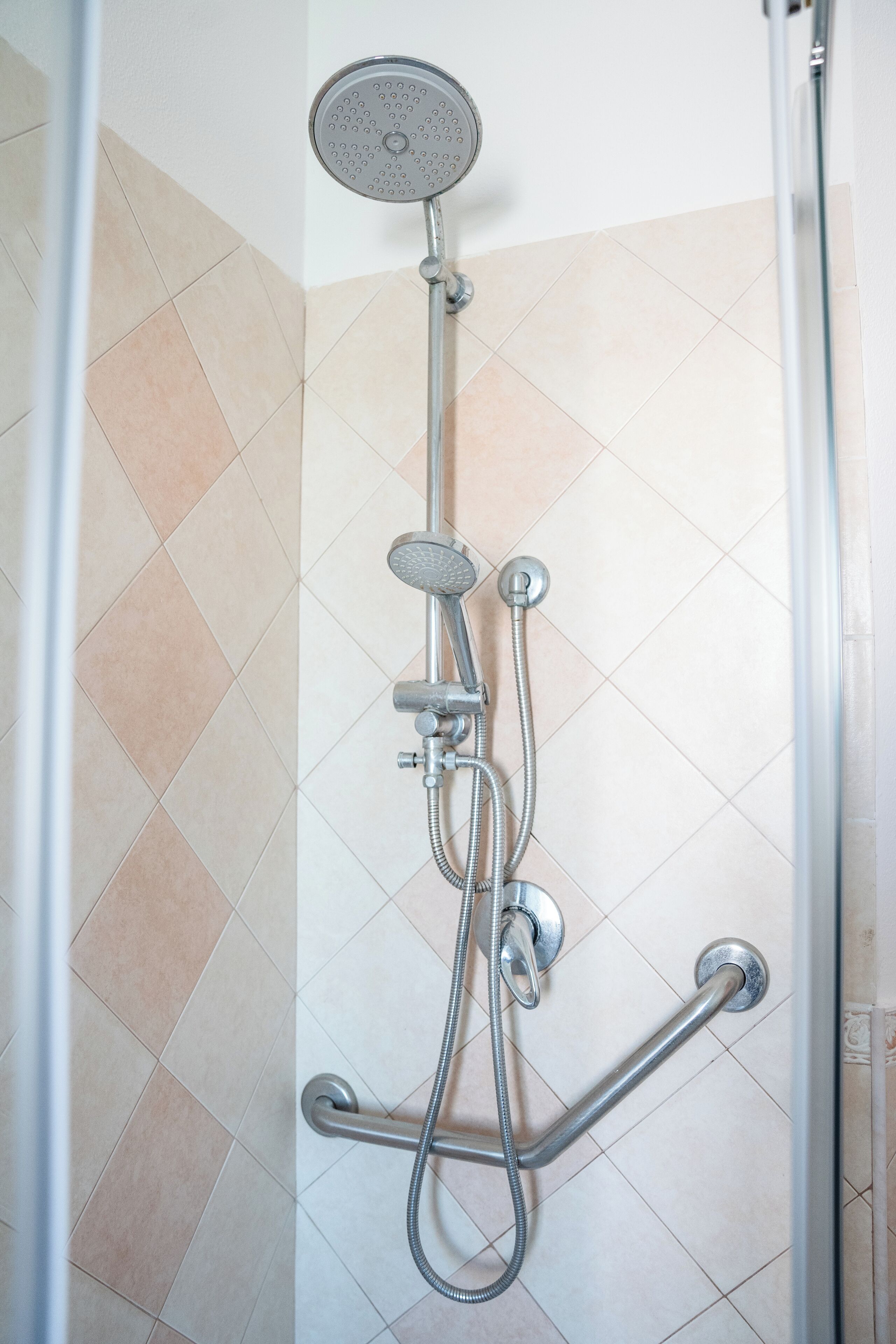 A shower with a handheld showerhead, a wall-mounted faucet, and a handheld hose.
