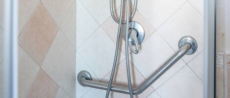 A shower with a handheld showerhead, a wall-mounted faucet, and a handheld hose.