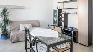 A modern living room with a glass-top dining table, a sofa, and a built-in bookshelf. - Casa Graziosa - Appartamento 5 (Nurachi)