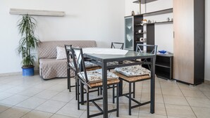 A modern living room with a glass-top dining table, black metal chairs, a beige sofa, and a wooden cabinet. - Casa Graziosa - Appartamento 5 (Nurachi)