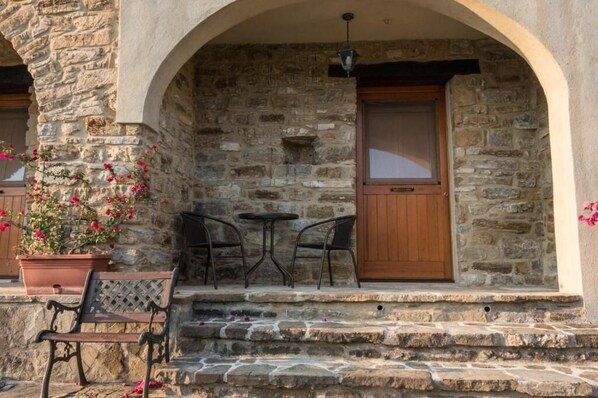 A stone building with a wooden door, a small table, two chairs, and a bench.