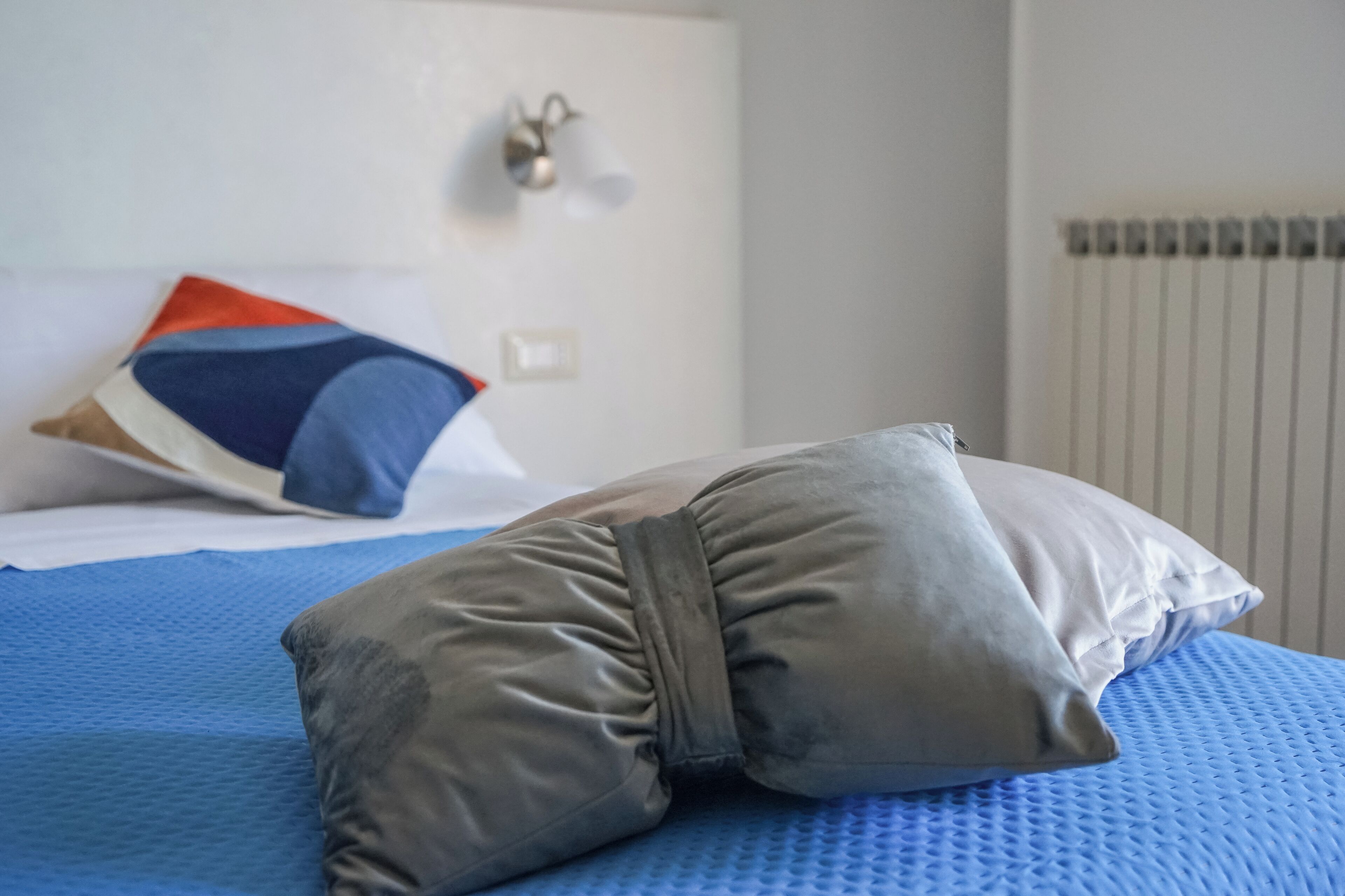 Una cama con un colchón azul, un almohadón gris y un cojín con diseño azul y naranja.