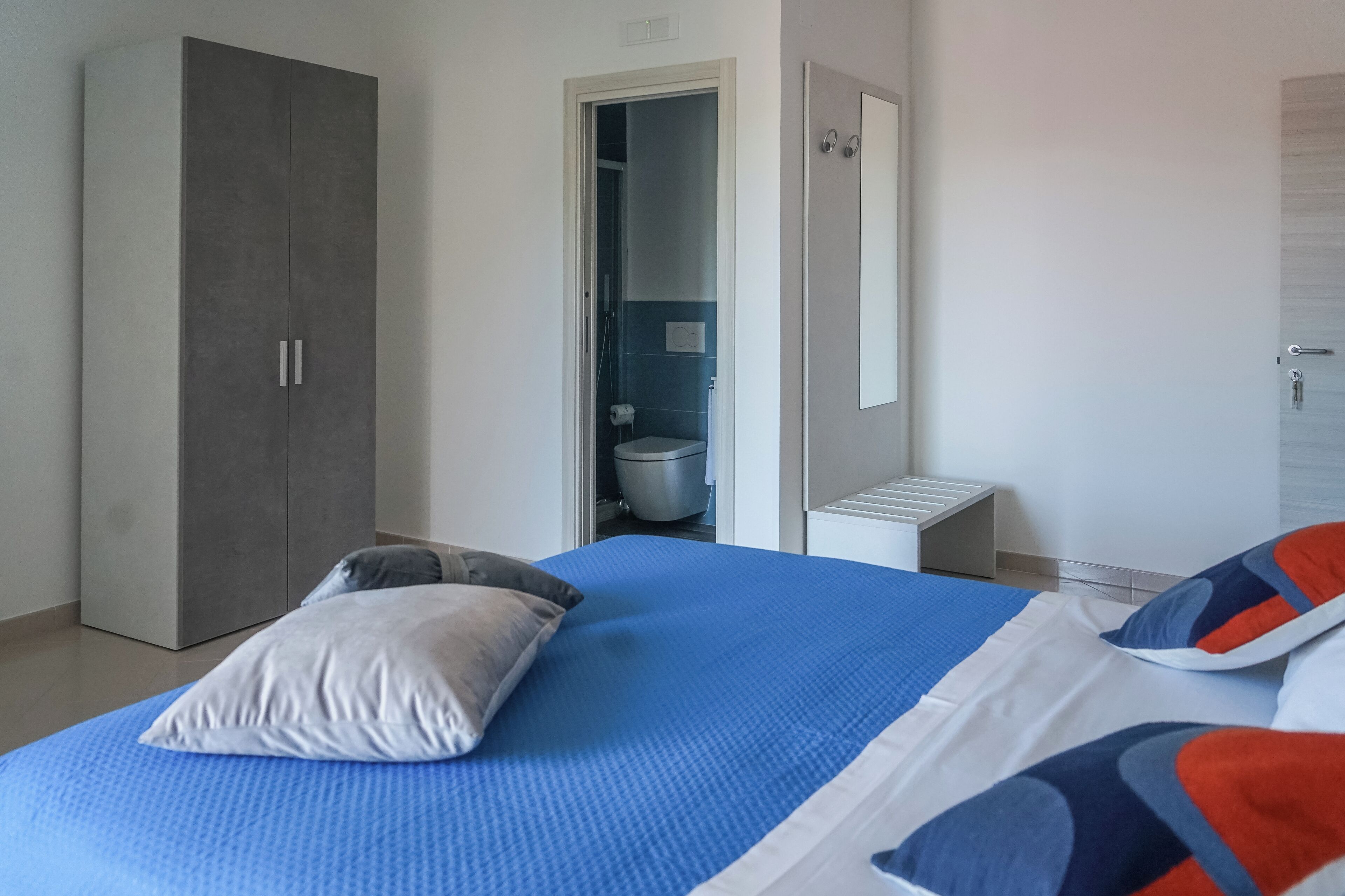 A bedroom with a bed, a wardrobe, a bathroom, and a small table.