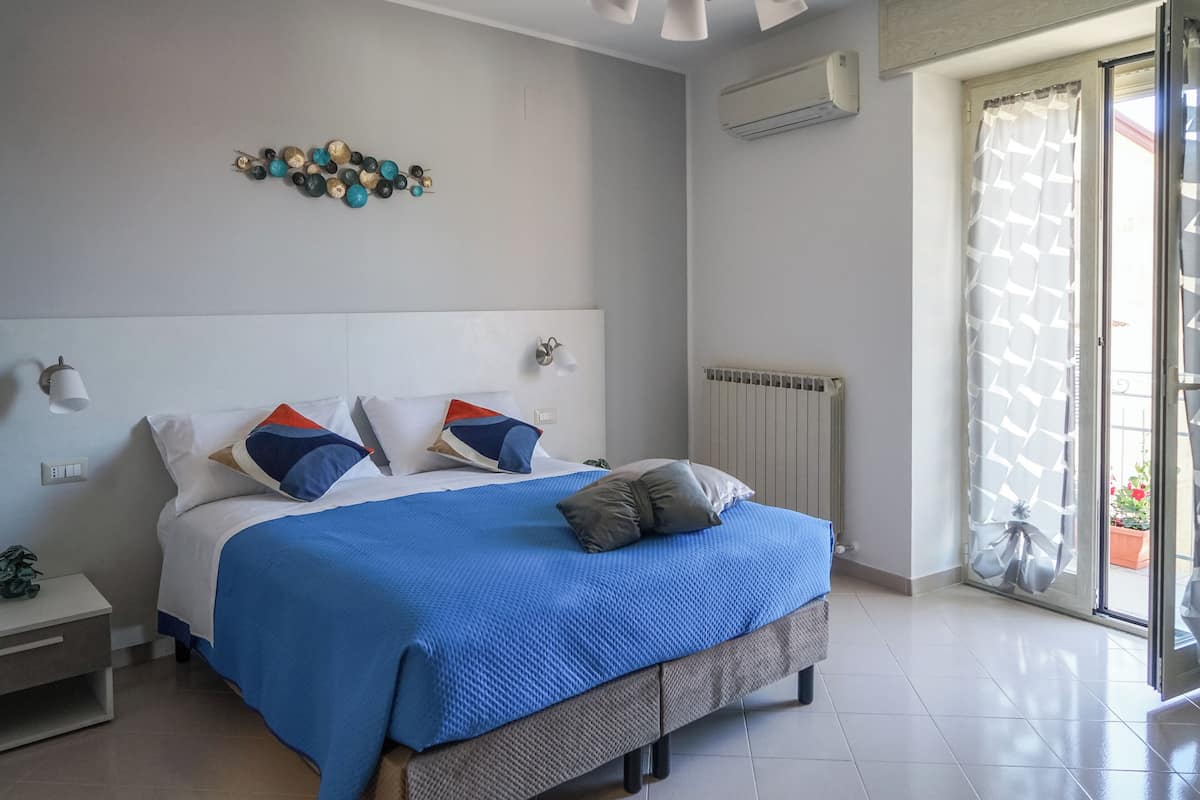 Un dormitorio con cama, mesitas de noche, aire acondicionado instalado en la pared y ventana con vistas al exterior.