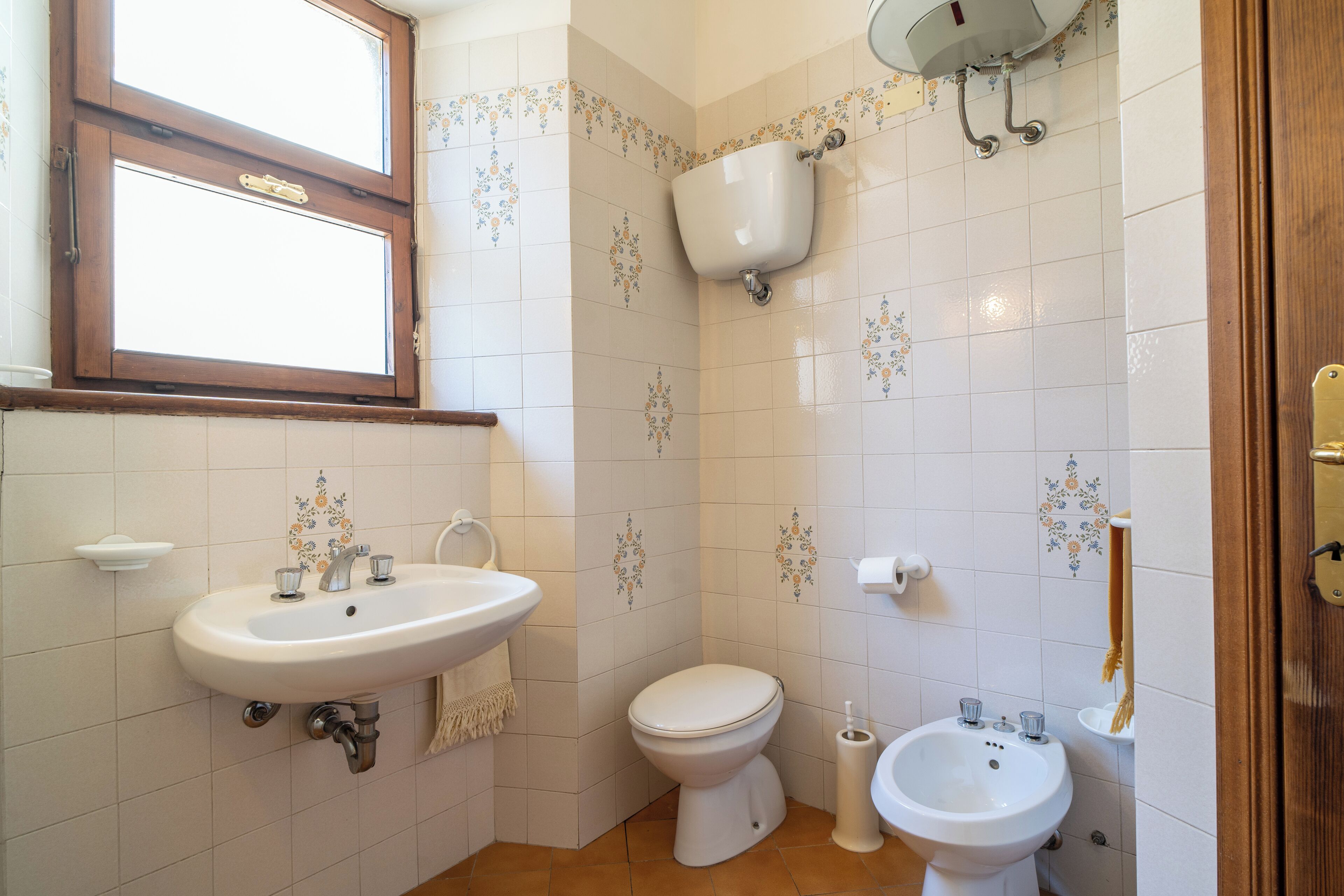 Een badkamer met een wastafel, toilet, bidet en een raam.