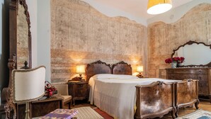 Une chambre à coucher de style traditionnel, avec un grand lit, une tête de lit en bois et un miroir. On y trouve deux tables de chevet avec des lampes, ainsi qu’une commode avec un miroir.
