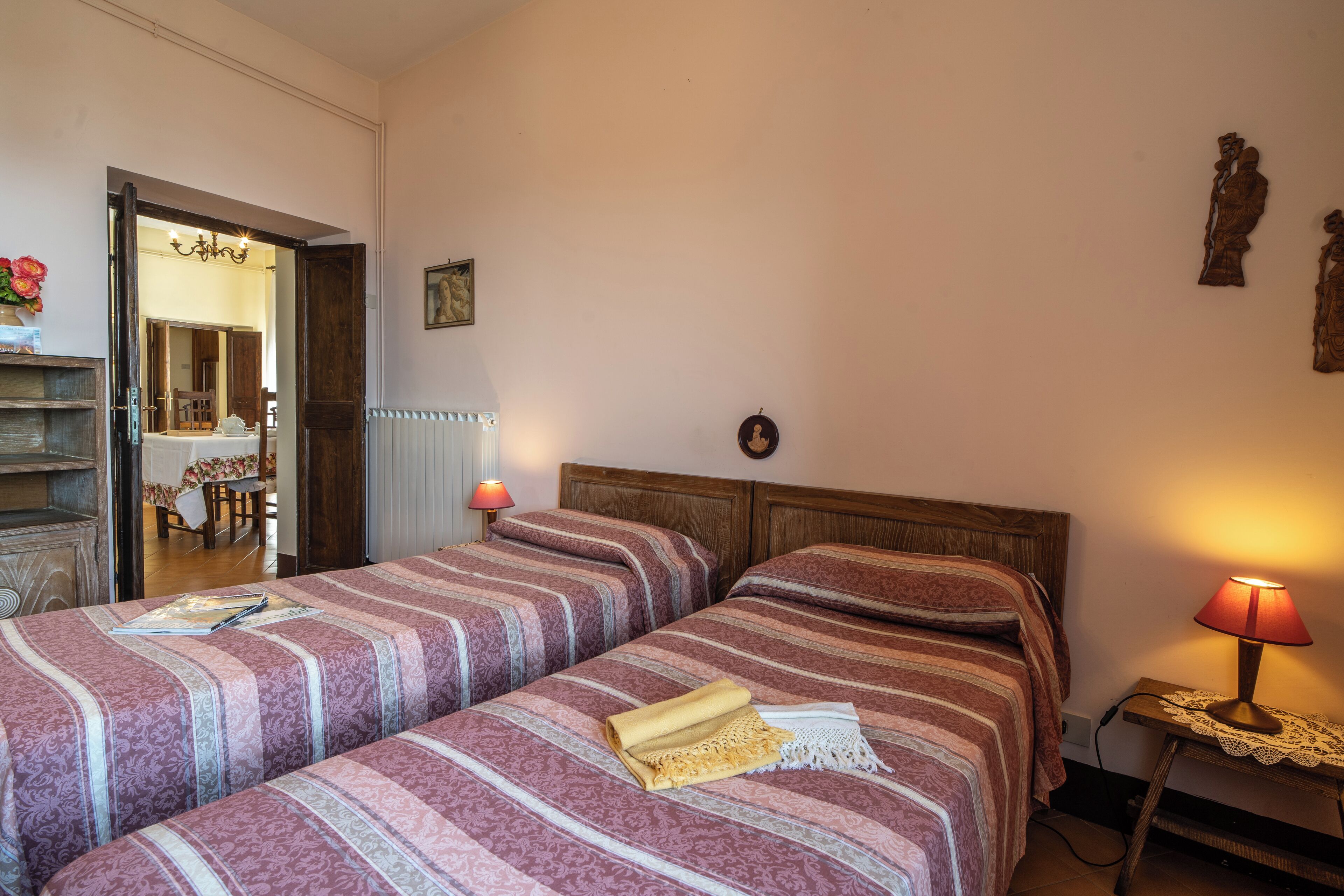 A bedroom with two beds, a wooden headboard, a bedside table with a lamp, and a door leading to a bathroom.