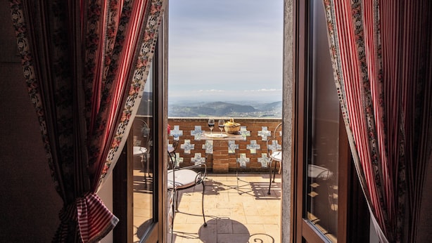 Une pièce avec vue sur les montagnes, accessible par une porte vitrée, comprenant une table avec des chaises et un rideau à motifs.